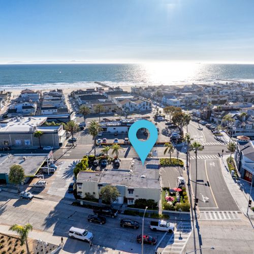 A coastal city with numerous buildings and streets near a beach overlooking the ocean, marked with a blue location pin.