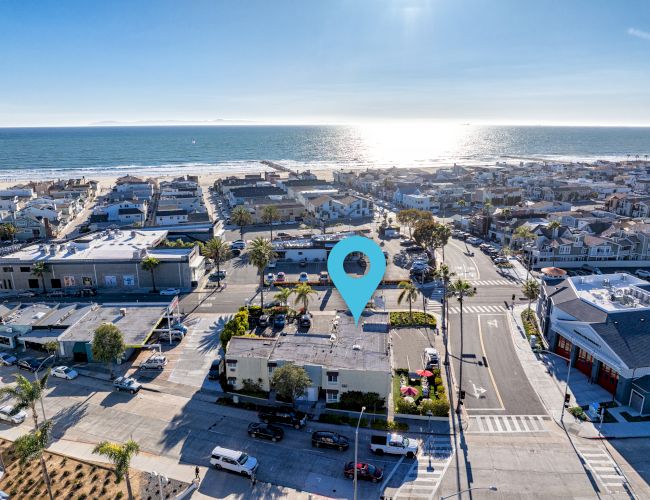 A coastal city with numerous buildings and streets near a beach overlooking the ocean, marked with a blue location pin.