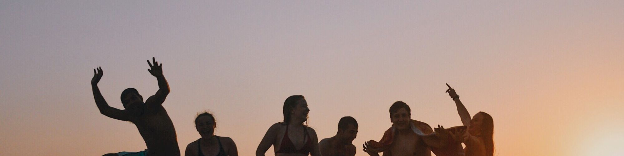 A group of people is having fun on the beach at sunset, with one person jumping joyfully.