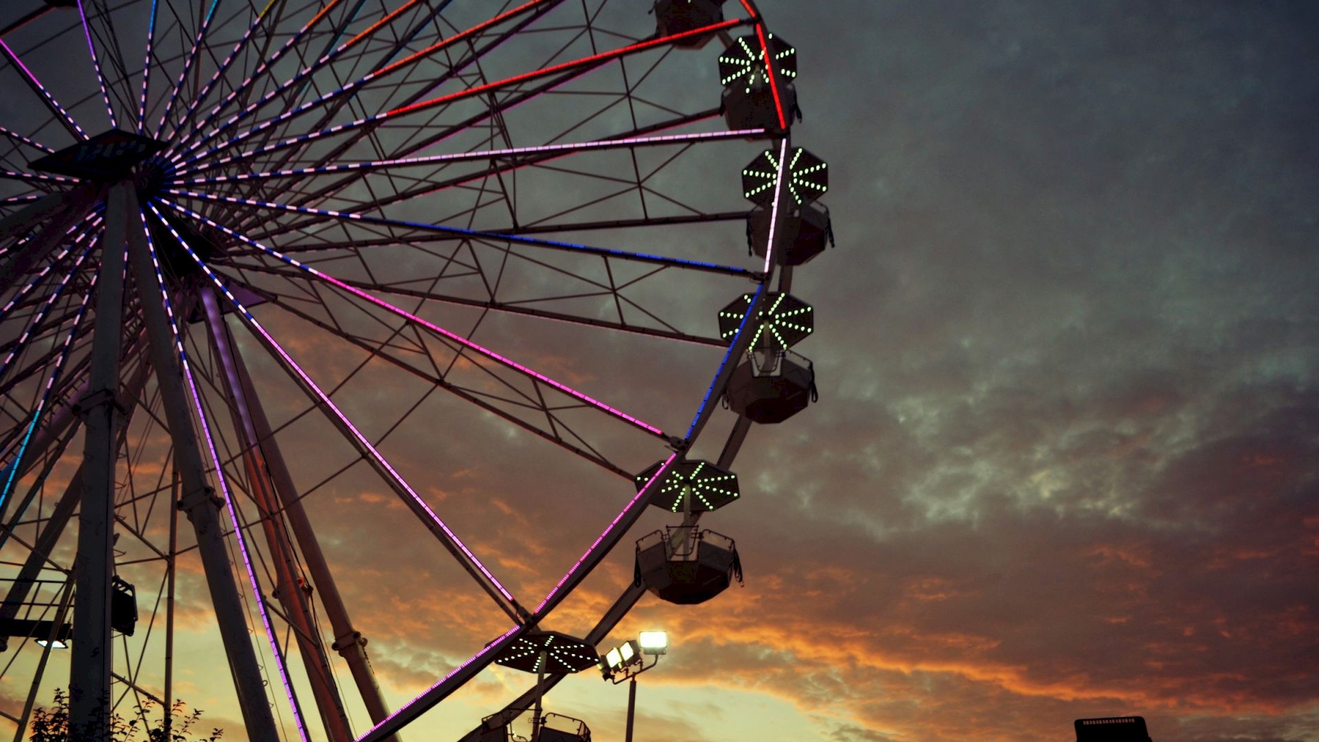 A Ferris wheel lit up with colorful lights stands against a dramatic sunset sky, creating a vibrant and picturesque scene.