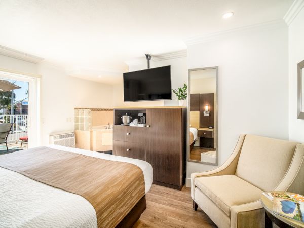 A cozy hotel room with a bed, TV, dresser, chair, and small seating area. There's a patio outside with an umbrella, hinting at an outdoor space.