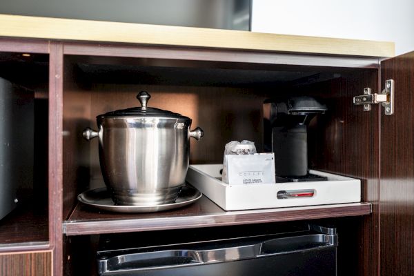 The image shows a cabinet containing a stainless steel ice bucket, a coffee maker, cups, and a refrigerator underneath.