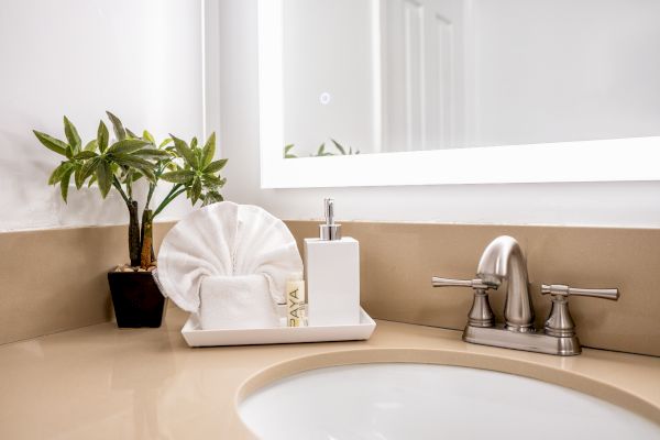 A bathroom sink area with a plant, decorative towel, soap dispenser, and a mirror. The countertop is beige, and the faucet is metallic, ending the sentence.