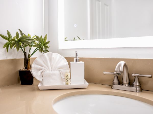 A bathroom sink area with a plant, decorative towel, soap dispenser, and a mirror. The countertop is beige, and the faucet is metallic, ending the sentence.