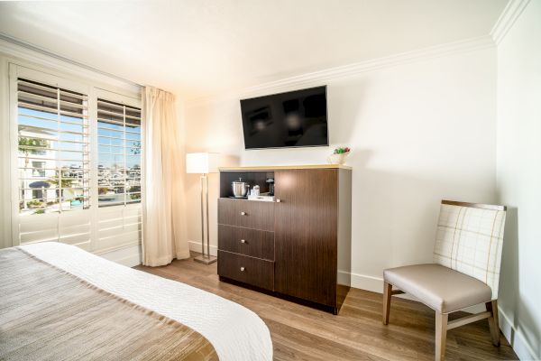 The image depicts a hotel room with a bed, a dresser with a TV, a chair, and a window with curtains.