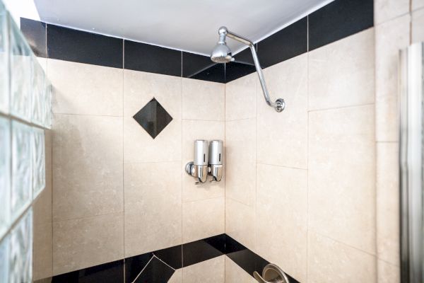 A tiled shower with beige and black tiles, featuring a showerhead and dual soap dispensers mounted on the wall.