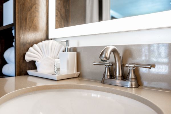 A bathroom sink with a chrome faucet, a soap dispenser, and neatly arranged towels on a tray, is featured in the image.