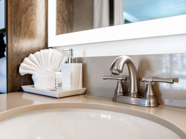 A bathroom sink with a chrome faucet, a soap dispenser, and neatly arranged towels on a tray, is featured in the image.