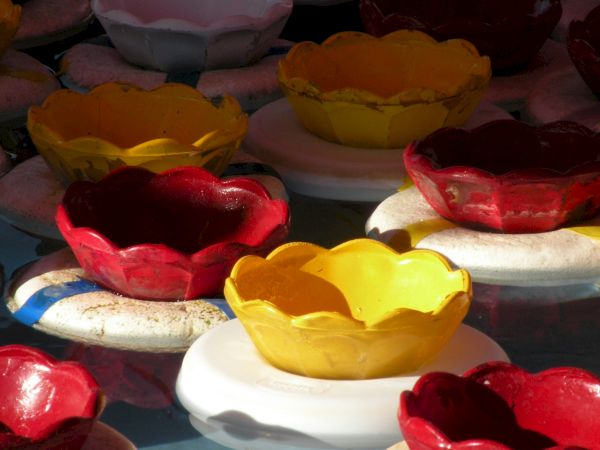 The image shows colorful floating flower-shaped bowls in red, yellow, and white, set on round white bases in a body of water, possibly for a festival.