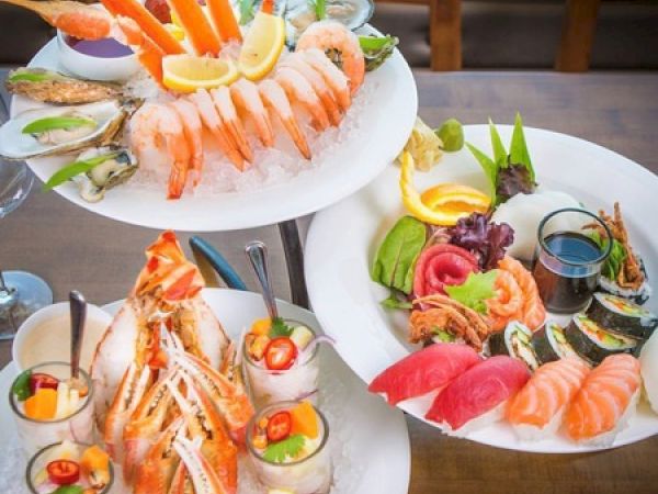 The image shows a variety of seafood dishes, including crab legs, shrimp, sushi, sashimi, and ceviche, all served with lemon and garnish on ice.