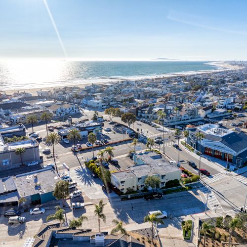 Aerial view of a coastal town featuring residential buildings, streets, beachfront, and a sunny ocean horizon.